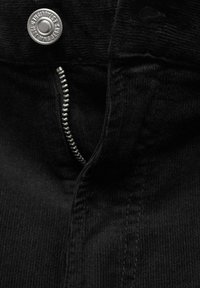 Tissu en velours côtelé noir avec une fermeture éclair visible et un bouton en métal. Texture côtelée verticale. Design minimaliste.