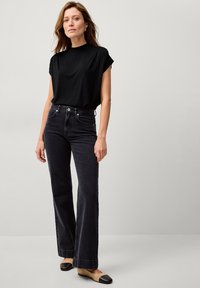 Sort kortærmet top med en afslappet pasform, parret med mørke højtaljede flared jeans. Skoene har et tofarvet design med en rund tå.