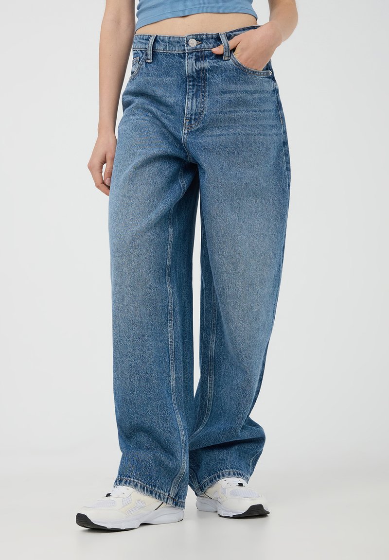 Jasnoniebieskie dżinsy z wysokim stanem o luźnym kroju, prostych nogawkach, wyblakłej teksturze, pięcioma kieszeniami oraz widocznymi detalami szycia.