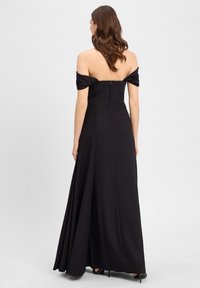 Schulterfreies schwarzes Kleid mit tailliertem Oberteil, weit auslaufendem Rock und Reißverschluss auf der Rückseite. Glattes, mattes Gewebe ohne sichtbare Muster.