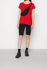 Rød kortærmet t-shirt, sorte cykelshorts, sort bæltetaske, sorte ankelstrømper og mørke træningssko; simpelt design og kontrasterende farver.