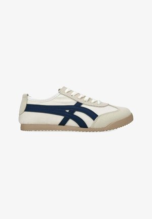 Zapatilla de lona blanca de perfil bajo con suela beige y rayas azul marino, con cordones blancos y detalles de ante en la puntera y el talón.