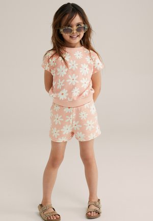 Roze bloemen kort set met korte mouwen, elastische tailleband en lichte muntkleurige madeliefjes; aangevuld met ronde zonnebril en tan sandalen.