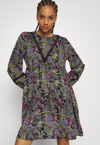 Vestido preto floral com mangas longas, decote em V com acabamento em contraste e uma silhueta solta e fluida adornada com flores coloridas.