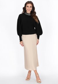 Maglione nero, peloso, con maniche a sbuffo e dettagli in perle sullo scollo, abbinato a una gonna beige, liscia, al ginocchio e sandali dorati con cinturino alla caviglia.