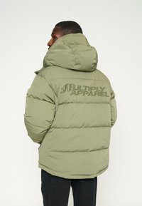 Oliven grøn pufferjakke med hætte, quiltet tekstur og "MULTIPLY APPAREL" logo i en mørkere grøn farve på ryggen.