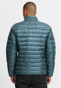 Gevoerde turquoise jas met een hoge kraag, voorzien van horizontale gestikte lijnen en een gladde, glanzende afwerking. De achterkant toont het ontwerp met elastische manchetten.