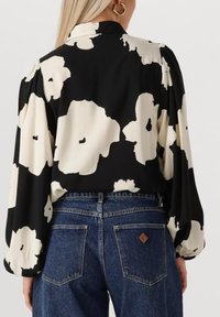Zwarte blouse met wit bloemmotief, met pofmouwen en een kraag, gecombineerd met blauw denim met hoge taille.