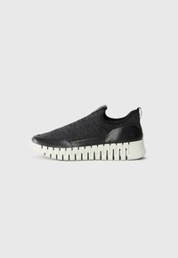 Black slip-on sneakers with a textured knit upper, rubber toe cap, and contrasting white ridged sole. No visible laces or closures.