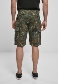 Pantalones cortos cargo con un patrón de camuflaje que presenta tonos de verde y marrón, con bolsillos laterales y un ajuste relajado. Fabricados con tela ligera.