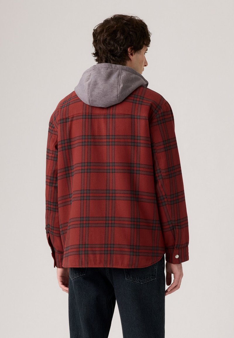 Czarna i czerwona koszula w kratę z szarym kapturem, charakteryzująca się luźnym krojem i guzikami przy mankietach. Miękka tkanina o lekko teksturowanym wyglądzie.