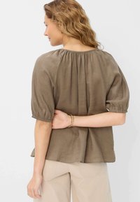 Blusa in lino marrone con scollatura arricciata e maniche a palloncino. Presenta una vestibilità morbida e delle pieghe laterali per un volume aggiuntivo. Design neutro.