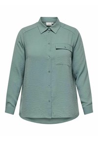 Košile s dlouhým rukávem, vyrobená z texturované látky světle zelené barvy, s límcem, jedinou náprsní kapsou a zakřiveným lemem.