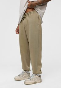 Beige sweatpants met elastische tailleband en trekkoord, voorzien van zijzakken en een losse pasvorm, gecombineerd met versleten witte sneakers.
