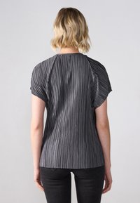 Top gri cu pliuri și mâneci scurte, având o textură ribbed și un design rotunjit pe spate, asortat cu pantaloni închiși la culoare.