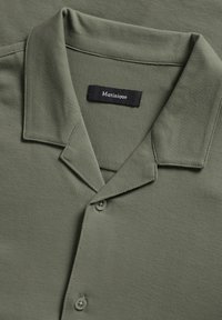 Camisa de manga corta color verde oliva con diseño de cuello, que presenta una textura suave, dos botones y una etiqueta cosida situada en el cuello.