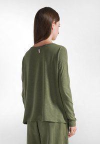 Langärmliges olivgrünes Oberteil aus einem weichen, strukturierten Stoff, mit rundem Ausschnitt und lässiger Passform, das ein kleines Etikett hinten hat.