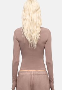 Langsleeve fitted top in lichtbruine stof, gladde textuur, ronde halslijn, gecombineerd met bijpassende broek met elastische tailleband.