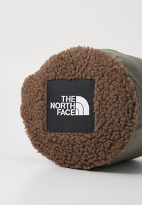 Brun fleece-futteret cirkulært enden af en grøn cylindrisk taske med et sort kvadratisk mærke, der viser den hvide The North Face-logo.