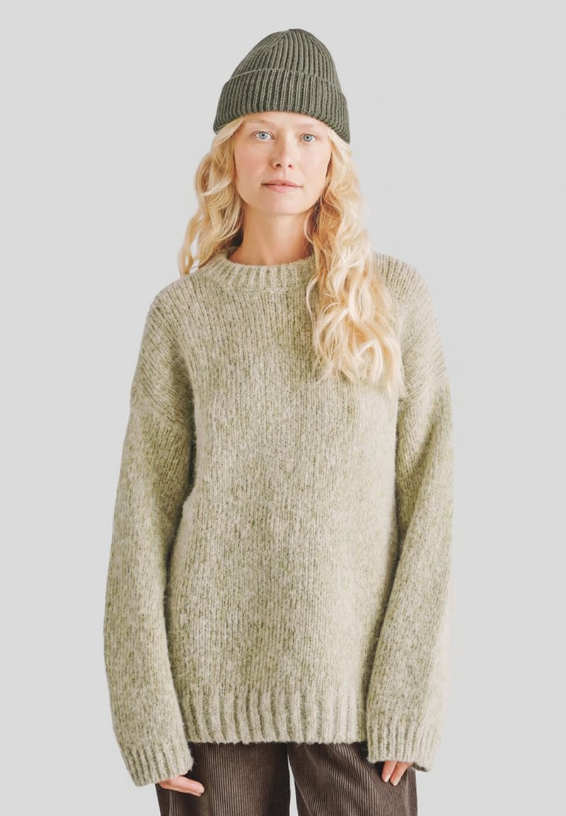 Jasnozielony, oversize'owy sweter z dzianiny z prążkowanym kołnierzem i mankietami, zestawiony z teksturowaną, ciemnozieloną czapką typu beanie. Miękka, gruba tkanina.