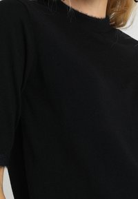Top de punto negro con un cuello alto y mangas hasta el codo, con un acabado suave y texturizado. Diseño simple y depurado sin patrones visibles.
