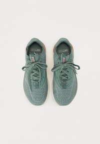 Scarpe sportive a rete verde con tomaia testurizzata, punte rotonde, lacci e accenti rosa sulla linguetta. Suola in gomma con un lieve tacco.