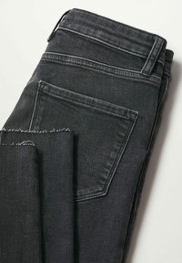 Paire de jeans en denim noir pliée montrant la poche arrière et le détail de l'ourlet brut sur la jambe sur un fond clair.