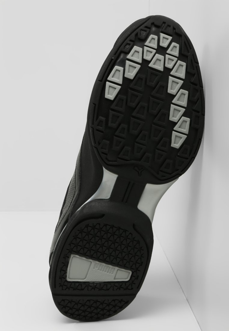 Zwarte sportieve schoen met een gestructureerde rubberen zool, voorzien van een geometrisch loopvlakpatroon en een zilveren accentlogo aan de zijkant.