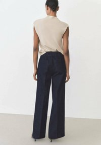 Beige ärmlös topp i kombination med högmidjade, vida mörka jeansbyxor. Byxorna har en strukturerad midjelinning och sidofickor.