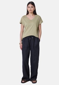 Khaki tričko s krátkým rukávem a výstřihem do V ve spojení s volnými džínovými kalhotami v námořnické modři. Významné detaily: stahovací pas a dvě přední kapsy.