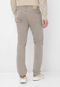 Beige Hosen mit schmaler Passform und subtiler Textur, ausgestattet mit zwei Gesäßtaschen und einem markierten Lederpatch am Bund.