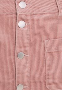 Rosa Cord-Stoff mit vertikalen Rillen, vier silberne Druckknöpfe mit der Bezeichnung "JDY DENIM" und einer gestickten quadratischen Tasche.