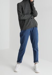 Ciemnoszary prążkowany golf zestawiony z luźnymi niebieskimi dżinsami i białymi trampkami. Prosty, swobodny strój z teksturowanej tkaniny.