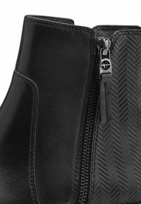 Schwarze Lederknöchelstiefel mit seitlichem Reißverschluss und Fischgrätenstruktur auf der Außenseite. Glatte Oberfläche mit dezenten Nähten.