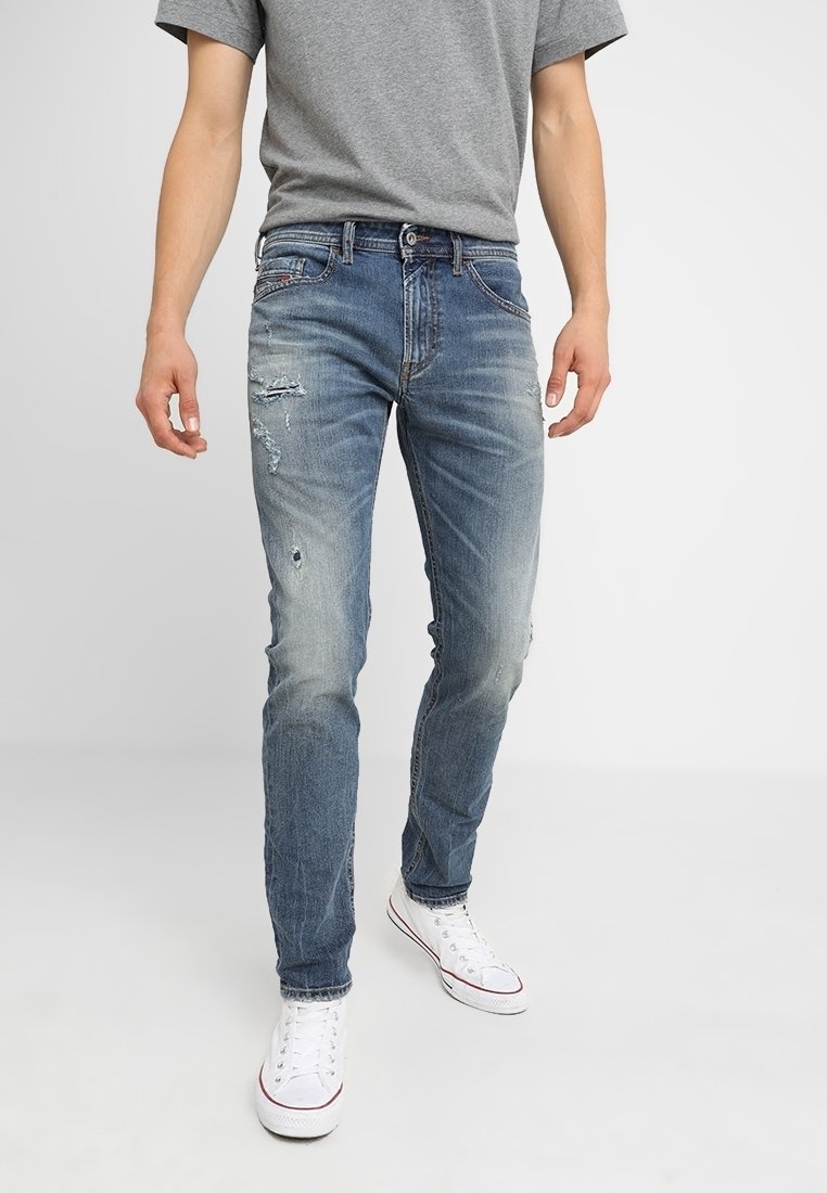 Blå slitna denimjeans med slim fit, med urtvättade sektioner och rivna detaljer, i kombination med en grå t-shirt och vita sneakers.