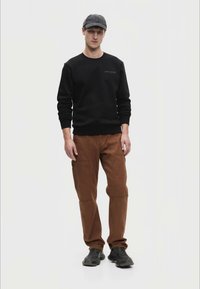 Fekete pulóver logóval,barna cargo nadrág oldalzsebekkel, fekete sportcipővel és szürke sapkával viselve. Egyszerű, funkcionális dizájn.