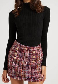 Sort ribbet langærmet top kombineret med et flerfarvet tweedskørt med ternet mønster og store, runde knapper foran.