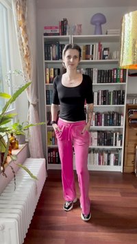 Black fitted top with short sleeves, pink sweatpants with pockets, and black and white sneakers. Background features bookshelves and plants.