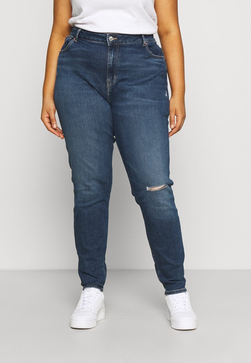 Mörkblå jeans i slim fit, med en slits vid knät, fem fickor och klassisk knappgylf. Kombinerade med vita sneakers.