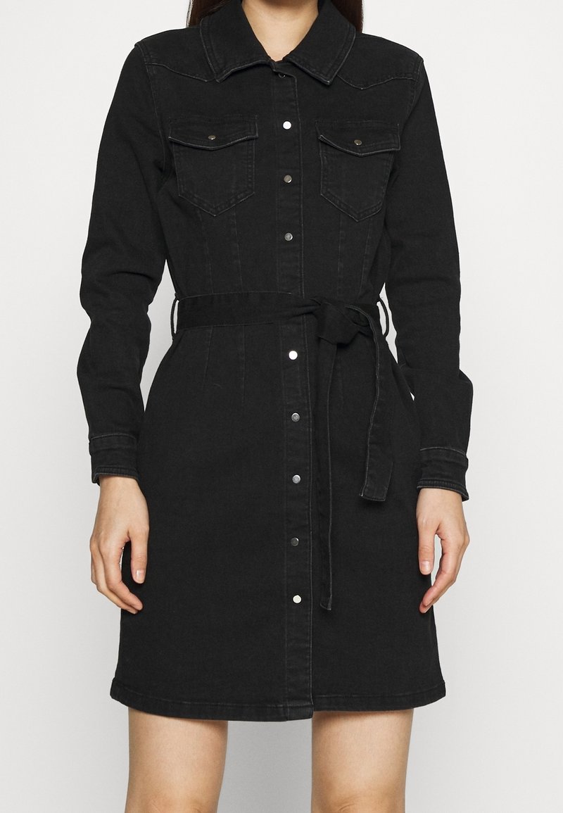 Svart denimskjortklänning med långa ärmar, knäppning fram, två bröstfickor och ett knytbälte i midjan för justerbar passform.