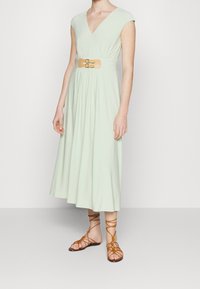 Světlězelené midi šaty s hlubokým výstřihem do V, krátkými rukávy a béžovým páskem se zlatou sponou. V kombinaci s hnědými sandály na řemínky.