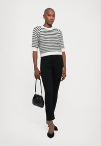 Gestreepte grijze en witte gebreide trui, zwarte strakke jeans, zwarte handtas en zwarte hakken. Zachte textuur, korte mouwen en cropped ontwerp.