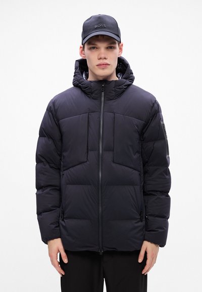 Veste noire matelassée avec zip à l'avant, capuche et plusieurs poches avant. Texture lisse avec une coupe moderne et une isolation légère.