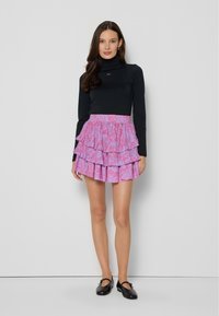 Zwarte lange mouwtop gecombineerd met een roze, gelaagde rok met ruffles met bloemenpatronen en een elastische tailleband. Model draagt zwarte flats.
