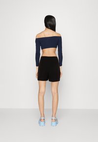 Námořnický off-the-shoulder crop top, černé šortky a světle modré platformové sandály. Hladká tkanina, přiléhavý střih, minimalistický styl.