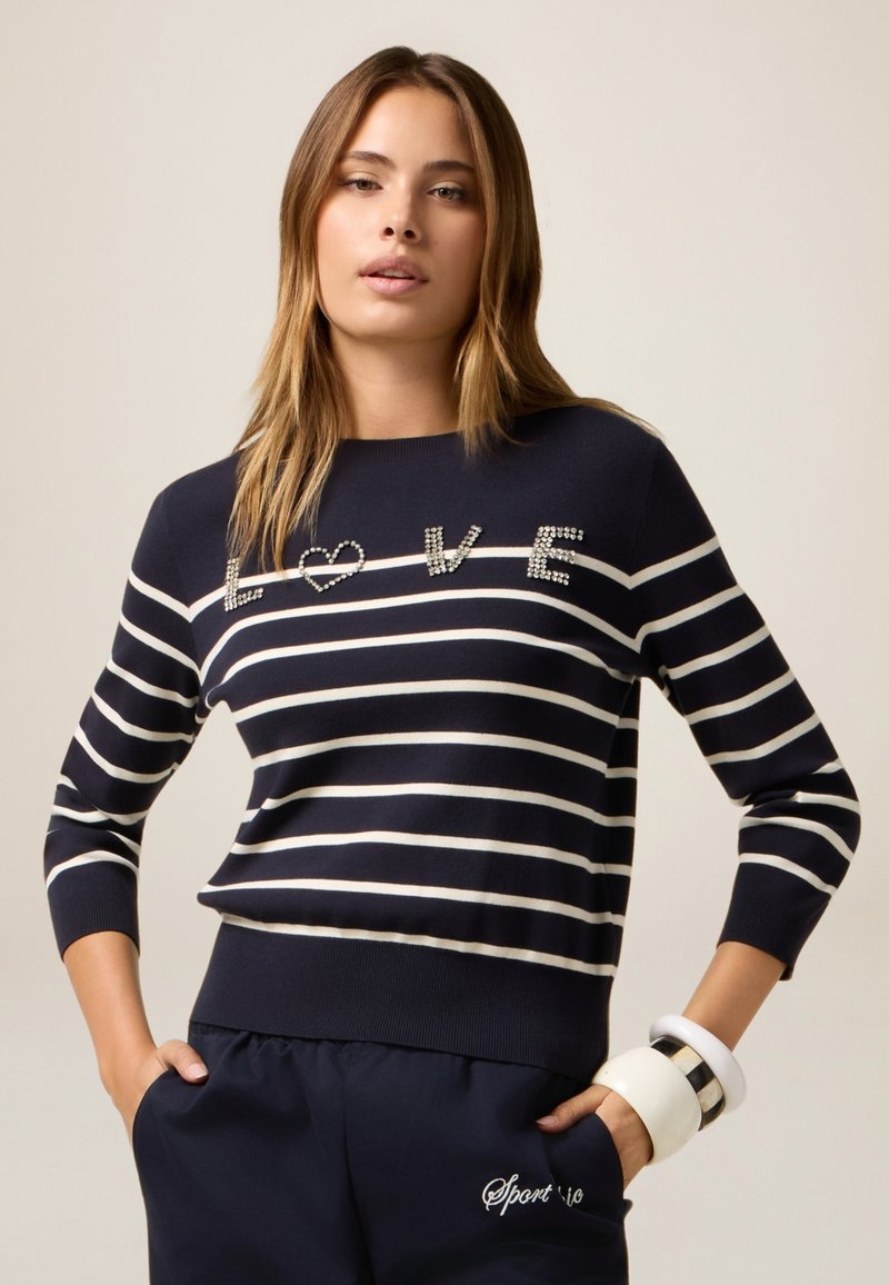 Maglione a righe navy con linee bianche, caratterizzato dal testo "LOVE" decorato sul davanti. Materiale morbido e design aderente con maniche a tre quarti.