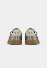 Sive metalne tenisice s glatkom teksturom, koje imaju bež akcentne boje i smešasti gumeni đon. Logo "VEJA" vidljiv na peti.