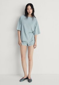 Maglietta oversized blu chiaro a maniche corte con pantaloni corti abbinati. Tessuto morbido e liscio con una vestibilità comoda. Scarpe scure con rifiniture viola.