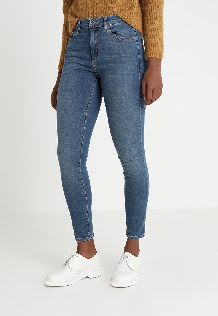 Tajta blå jeans i denim, med hög midja, fem fickor och diskret sömnad. Kombinerade med vita skor.