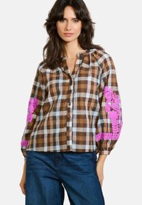 Camicia a quadri marrone e bianca con ricami floreali rosa sulle maniche, completata da un davanti con bottoni e una vestibilità rilassata.